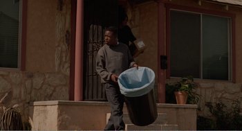 Movie still from “Menace II Society” (1993), directed by Albert Hughes – A man carrying a trash can down the stairs; Medium shot, Low angle