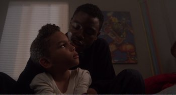 Movie still from “Menace II Society” (1993), directed by Albert Hughes – A man and a boy sitting on a couch; Close Up shot, Over the shoulder angle