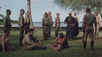 Movie still from “Merry Christmas Mr. Lawrence” (1983), directed by Nagisa Ôshima – A group of men standing next to each other on the grass; Wide shot, High angle