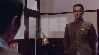 Movie still from “Merry Christmas Mr. Lawrence” (1983), directed by Nagisa Ôshima – A man in a uniform standing in front of a window; Medium shot, Low angle