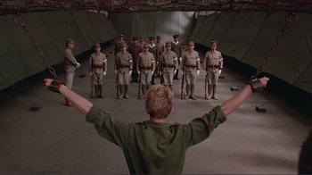Movie still from “Merry Christmas Mr. Lawrence” (1983), directed by Nagisa Ôshima – A group of men standing in formation in front of a man with his hands up; Wide shot, Low angle