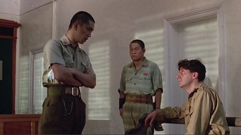 Movie still from “Merry Christmas Mr. Lawrence” (1983), directed by Nagisa Ôshima – A group of men standing next to each other in a room; Medium shot, Over the shoulder angle