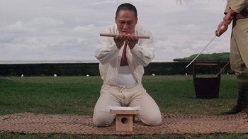 Movie still from “Merry Christmas Mr. Lawrence” (1983), directed by Nagisa Ôshima – A man kneeling down on the ground holding a wooden stick; Medium shot, Low angle