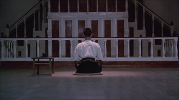 Movie still from “Merry Christmas Mr. Lawrence” (1983), directed by Nagisa Ôshima – A man sitting on the ground in front of a wall; Wide shot, High angle