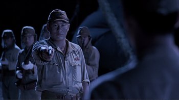 Movie still from “Merry Christmas Mr. Lawrence” (1983), directed by Nagisa Ôshima – A man pointing at something in a dark room; Medium shot, Over the shoulder angle