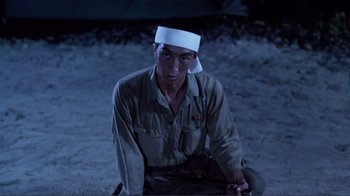 Movie still from “Merry Christmas Mr. Lawrence” (1983), directed by Nagisa Ôshima – A man with a white hat sitting on the ground; Medium shot, Low angle