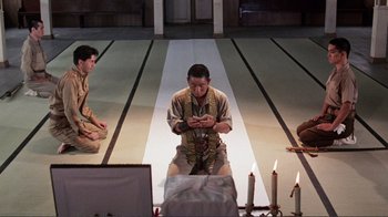 Movie still from “Merry Christmas Mr. Lawrence” (1983), directed by Nagisa Ôshima – A man kneeling on the ground in front of candles; Wide shot, High angle