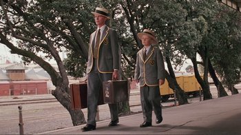 Movie still from “Merry Christmas Mr. Lawrence” (1983), directed by Nagisa Ôshima – A man and a boy are walking down the sidewalk; Wide shot, Low angle