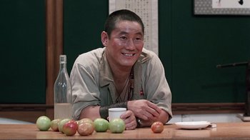 Movie still from “Merry Christmas Mr. Lawrence” (1983), directed by Nagisa Ôshima – A man sitting in front of a table with apples; Close Up shot, Over the shoulder angle