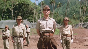Movie still from “Merry Christmas Mr. Lawrence” (1983), directed by Nagisa Ôshima – A group of men standing next to each other on top of a dirt field; Medium shot, Low angle
