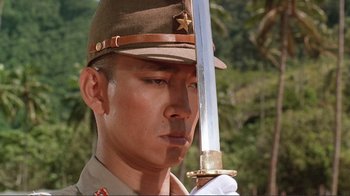 Movie still from “Merry Christmas Mr. Lawrence” (1983), directed by Nagisa Ôshima – A man in a uniform holding a sword in his hand; Close Up shot, Low angle
