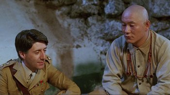 Movie still from “Merry Christmas Mr. Lawrence” (1983), directed by Nagisa Ôshima – Two men sitting next to each other in front of a stone wall; Close Up shot, Over the shoulder angle