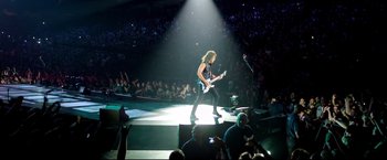 Movie still from “Metallica Through the Never” (2013), directed by Nimród Antal – A man in a black shirt is playing guitar; Wide shot, High angle