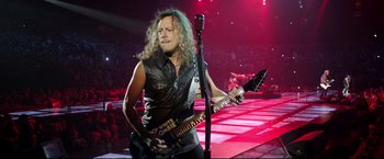 Movie still from “Metallica Through the Never” (2013), directed by Nimród Antal – A man in leather vest holding a guitar and a microphone; Medium shot, Low angle