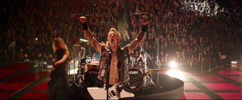 Movie still from “Metallica Through the Never” (2013), directed by Nimród Antal – A man in a black vest is on a stage; Wide shot, Overhead angle
