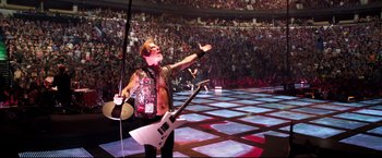 Movie still from “Metallica Through the Never” (2013), directed by Nimród Antal – A man holding a guitar in front of an audience; Wide shot, High angle