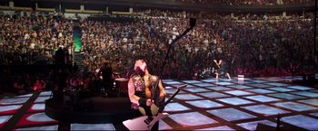 Movie still from “Metallica Through the Never” (2013), directed by Nimród Antal – A man sitting on a stage holding a guitar; Extreme Wide shot, High angle