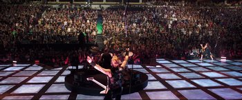 Movie still from “Metallica Through the Never” (2013), directed by Nimród Antal – A man in a crowd of people holding a microphone; Extreme Wide shot, High angle