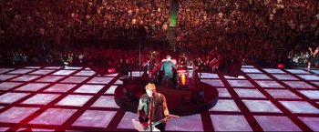 Movie still from “Metallica Through the Never” (2013), directed by Nimród Antal – A man holding a guitar while standing in front of an audience; Extreme Wide shot, High angle