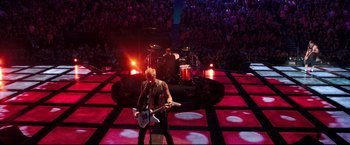 Movie still from “Metallica Through the Never” (2013), directed by Nimród Antal – A man with a guitar on a stage; Extreme Wide shot, Overhead angle