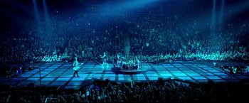 Movie still from “Metallica Through the Never” (2013), directed by Nimród Antal – A crowd of people watching a band perform on a stage; Extreme Wide shot, High angle