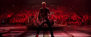 Movie still from “Metallica Through the Never” (2013), directed by Nimród Antal – A man with a guitar in front of an audience; Wide shot, Overhead angle