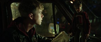 A man sitting in the driver's seat of a car reading a newspaper