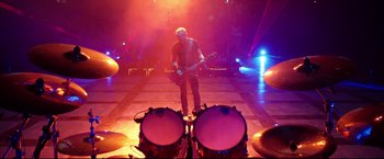Movie still from “Metallica Through the Never” (2013), directed by Nimród Antal – A man with a guitar standing in front of two drums; Wide shot, Low angle