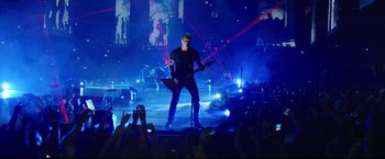 Movie still from “Metallica Through the Never” (2013), directed by Nimród Antal – A man in black shirt holding a guitar on a stage; Wide shot, Low angle