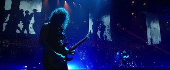 Movie still from “Metallica Through the Never” (2013), directed by Nimród Antal – A man playing a guitar on a stage in front of an audience; Wide shot, Low angle