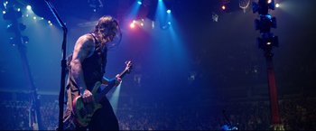 Movie still from “Metallica Through the Never” (2013), directed by Nimród Antal – A person playing a guitar in a dark room; Wide shot, High angle