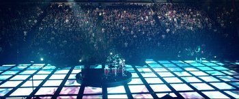 Movie still from “Metallica Through the Never” (2013), directed by Nimród Antal – A drum set is on a stage in front of a crowd; Extreme Wide shot, High angle