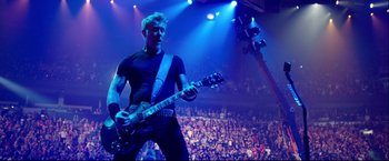 Movie still from “Metallica Through the Never” (2013), directed by Nimród Antal – A man in a black shirt is playing a guitar in front of an audience; Medium shot, Low angle