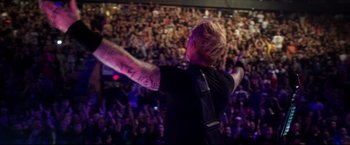 Movie still from “Metallica Through the Never” (2013), directed by Nimród Antal – A man with a tattoo on his arm is on a stage; Wide shot, High angle