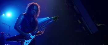 Movie still from “Metallica Through the Never” (2013), directed by Nimród Antal – A person playing a guitar in a dark room; Medium shot, Low angle
