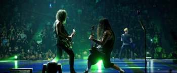 Movie still from “Metallica Through the Never” (2013), directed by Nimród Antal – A couple of men on stage with a guitar; Wide shot, High angle