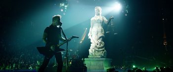 Movie still from “Metallica Through the Never” (2013), directed by Nimród Antal – A man playing a guitar in front of a statue of lady justice; Wide shot, Low angle