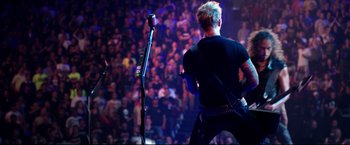 Movie still from “Metallica Through the Never” (2013), directed by Nimród Antal – A man in a black t - shirt is playing a guitar; Wide shot, High angle