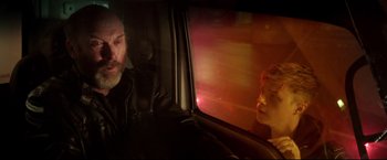 A man sitting in a car looking out the window at a woman