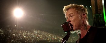Movie still from “Metallica Through the Never” (2013), directed by Nimród Antal – A man is speaking into a microphone in front of an audience; Close Up shot, Low angle