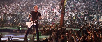 Movie still from “Metallica Through the Never” (2013), directed by Nimród Antal – A man playing a guitar in front of a large crowd; Wide shot, High angle