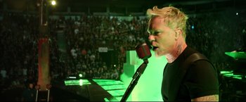 Movie still from “Metallica Through the Never” (2013), directed by Nimród Antal – A man with blond hair is singing into a microphone at an event; Close Up shot, High angle