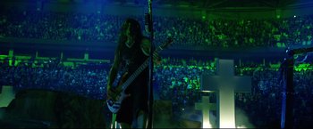 Movie still from “Metallica Through the Never” (2013), directed by Nimród Antal – A man with long black hair playing a guitar in front of an audience; Wide shot, High angle
