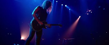 Movie still from “Metallica Through the Never” (2013), directed by Nimród Antal – A man with curly hair is playing a guitar on a stage; Medium shot, Low angle