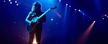 Movie still from “Metallica Through the Never” (2013), directed by Nimród Antal – A man with a long curly hair is playing a guitar; Wide shot, Low angle