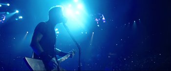 Movie still from “Metallica Through the Never” (2013), directed by Nimród Antal – A person playing a guitar in a dark room; Medium shot, Low angle