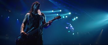 Movie still from “Metallica Through the Never” (2013), directed by Nimród Antal – A man holding a microphone and a guitar; Medium shot, Low angle