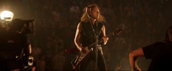 Movie still from “Metallica Through the Never” (2013), directed by Nimród Antal – A man in a black leather vest is playing a guitar; Medium shot, Low angle