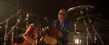 Movie still from “Metallica Through the Never” (2013), directed by Nimród Antal – A man is playing drums in a dark room; Medium shot, High angle