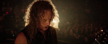 Movie still from “Metallica Through the Never” (2013), directed by Nimród Antal – A man with curly hair is standing in a dark room; Close Up shot, High angle
